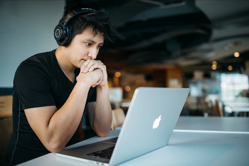 Man with headphones staring at Apple Laptop