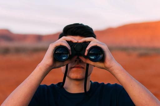 A man holding binoculars up to his eyes with a desert behind him